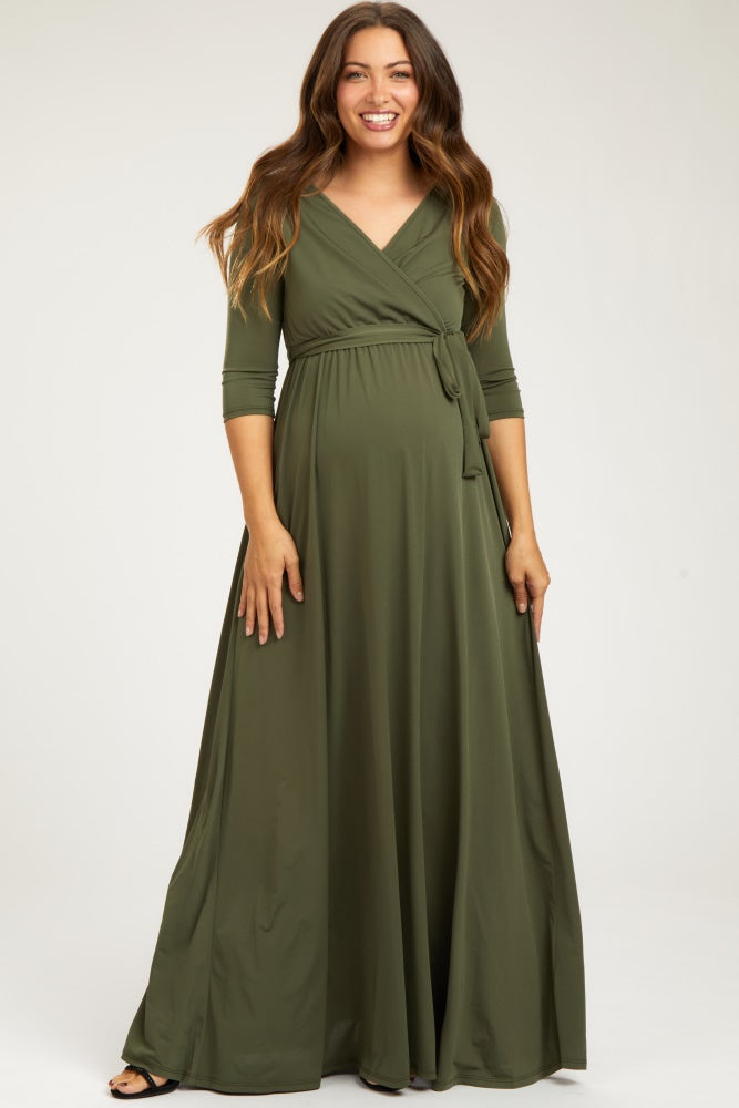 woman wearing a dark green maternity wrap maxi dress with three-quarter sleeves and a tied waist, standing and smiling