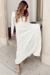 woman wearing a white long sleeve maxi dress and standing on a step, holding the hem of her dress