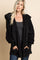 woman wearing a black fluffy oversized jacket over a white crop top against a green background
