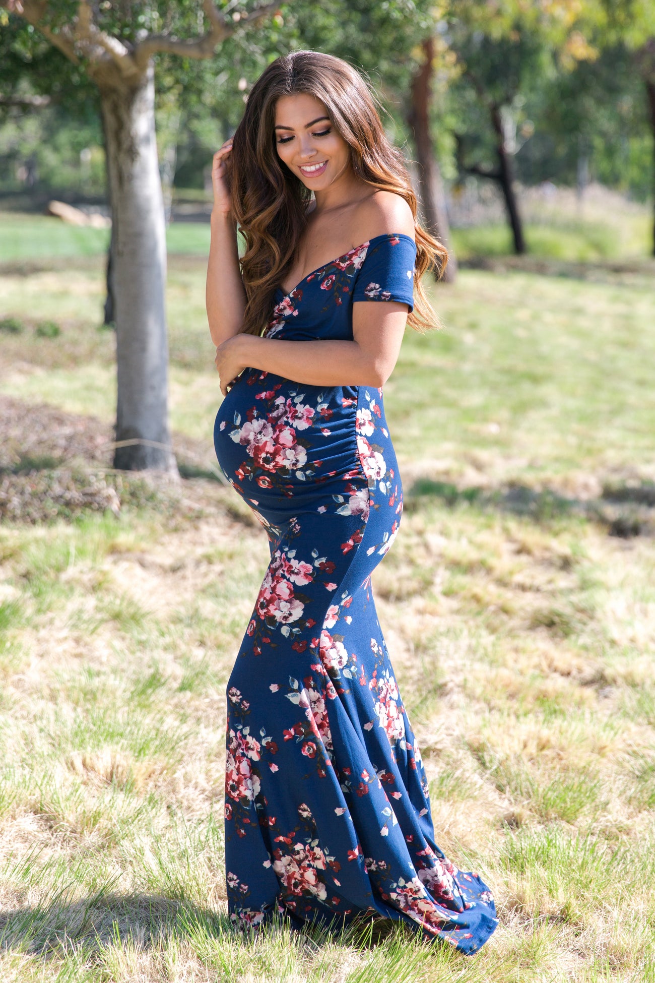 pregnant woman in blue floral off-the-shoulder maternity maxi dress standing in a park