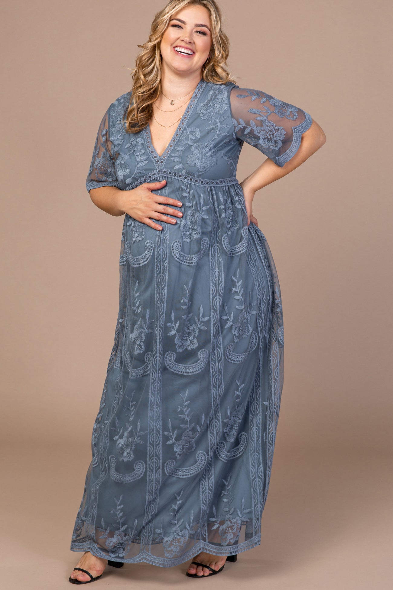 woman wearing a gray lace maternity maxi dress with short sleeves, smiling and showing her baby bump