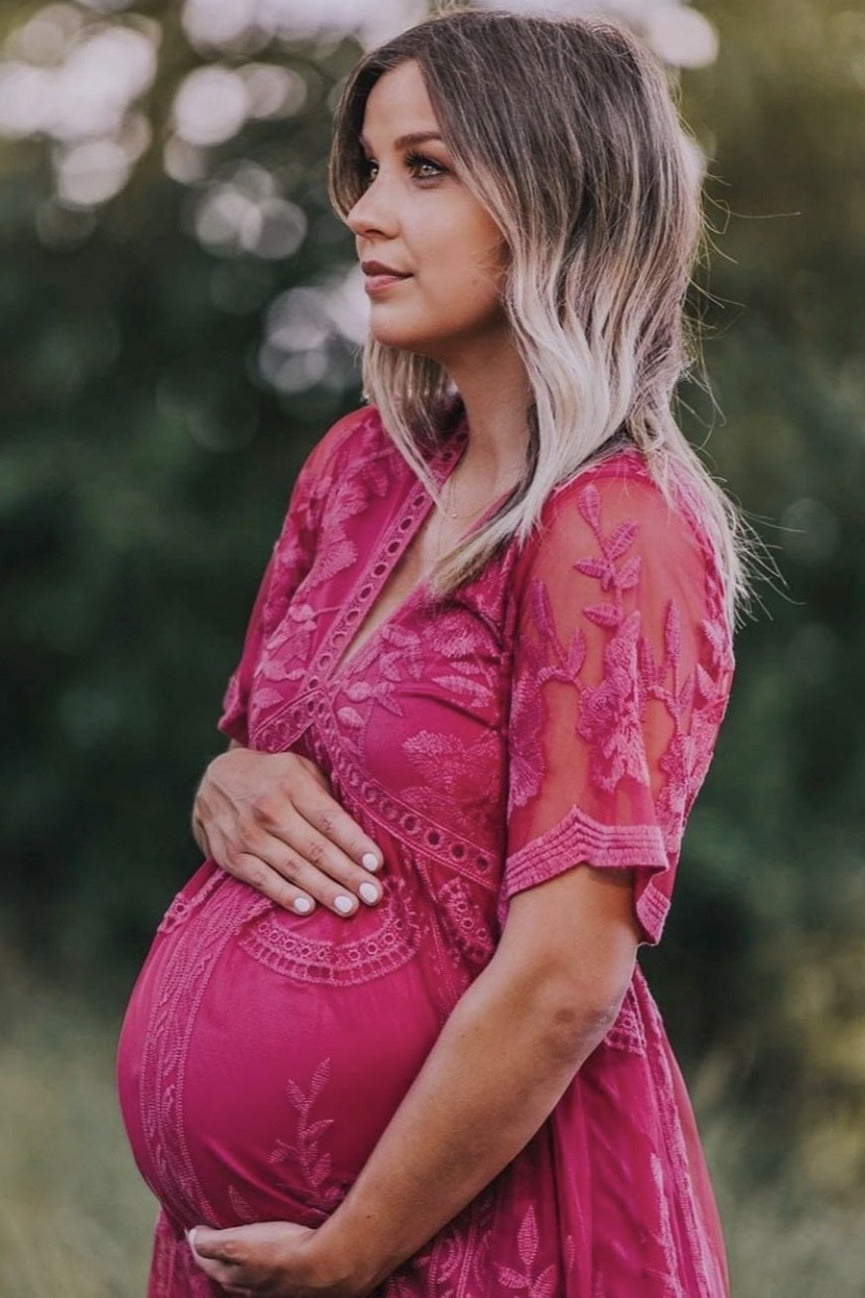 woman wearing a pink embroidered maternity dress and holding her baby bump