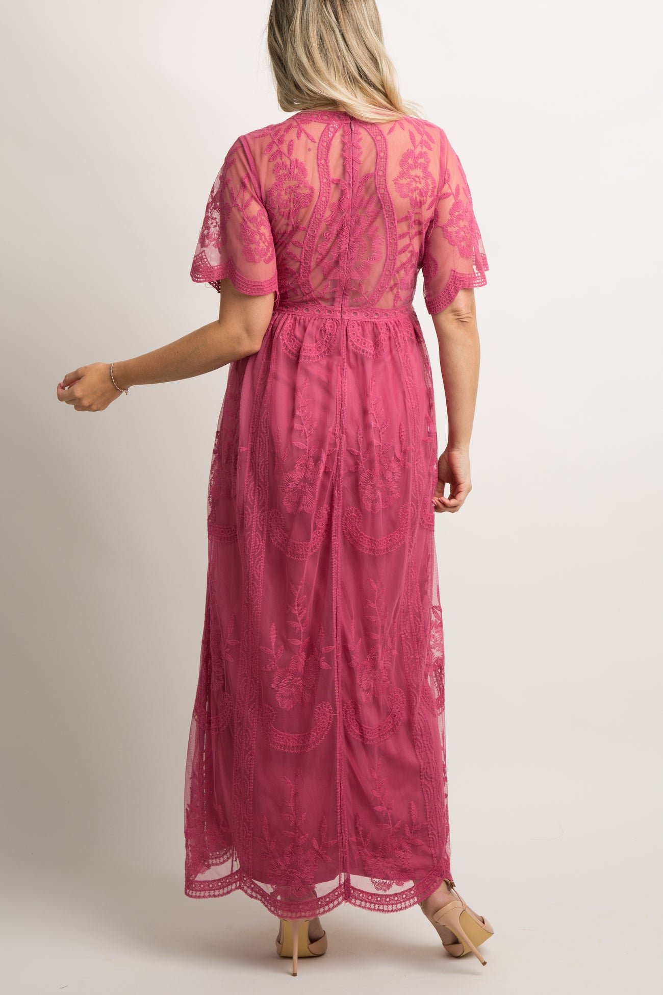 woman wearing a burgundy maternity maxi dress with floral lace details and a visible baby bump