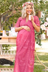 woman wearing a pink embroidered maternity maxi dress, holding a drink and showing her baby bump with a floral crown on her head