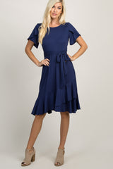 blonde woman wearing a navy blue short sleeve ruffle hem dress with a waist tie and tan heels