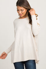 smiling pregnant woman wearing a cream long sleeve maternity tunic sweater and dark jeans