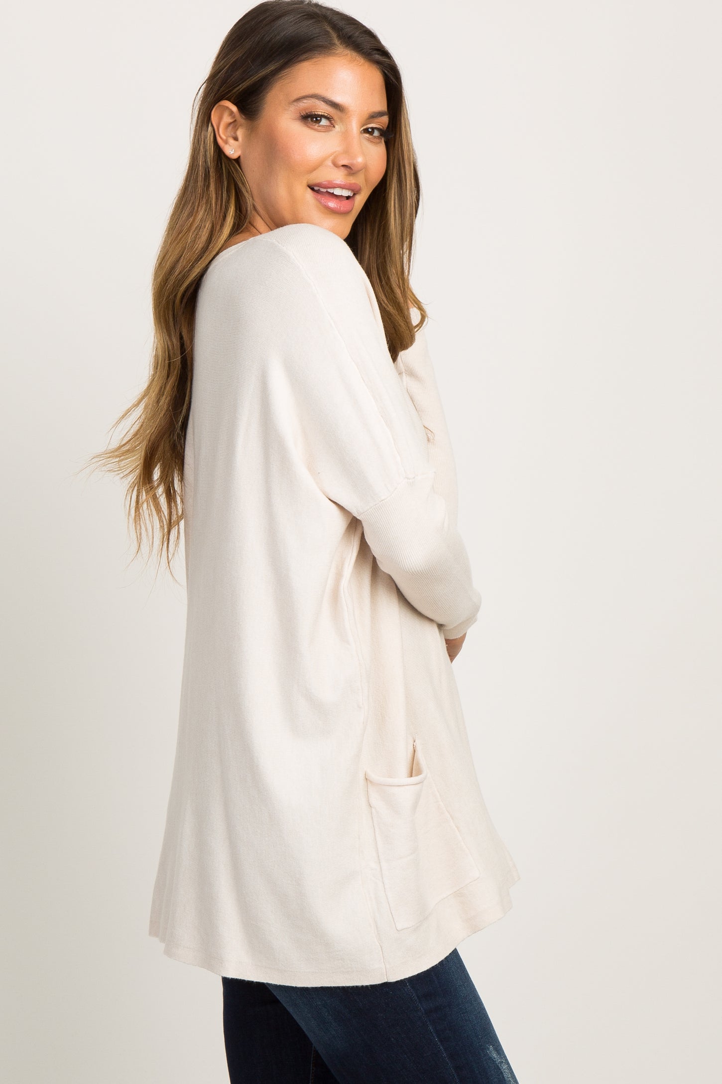 pregnant woman in a cream long sleeve maternity tunic top with pockets standing against a white background