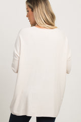 Back view of a woman wearing an oversized cream knit sweater with drop shoulders and ribbed cuffs