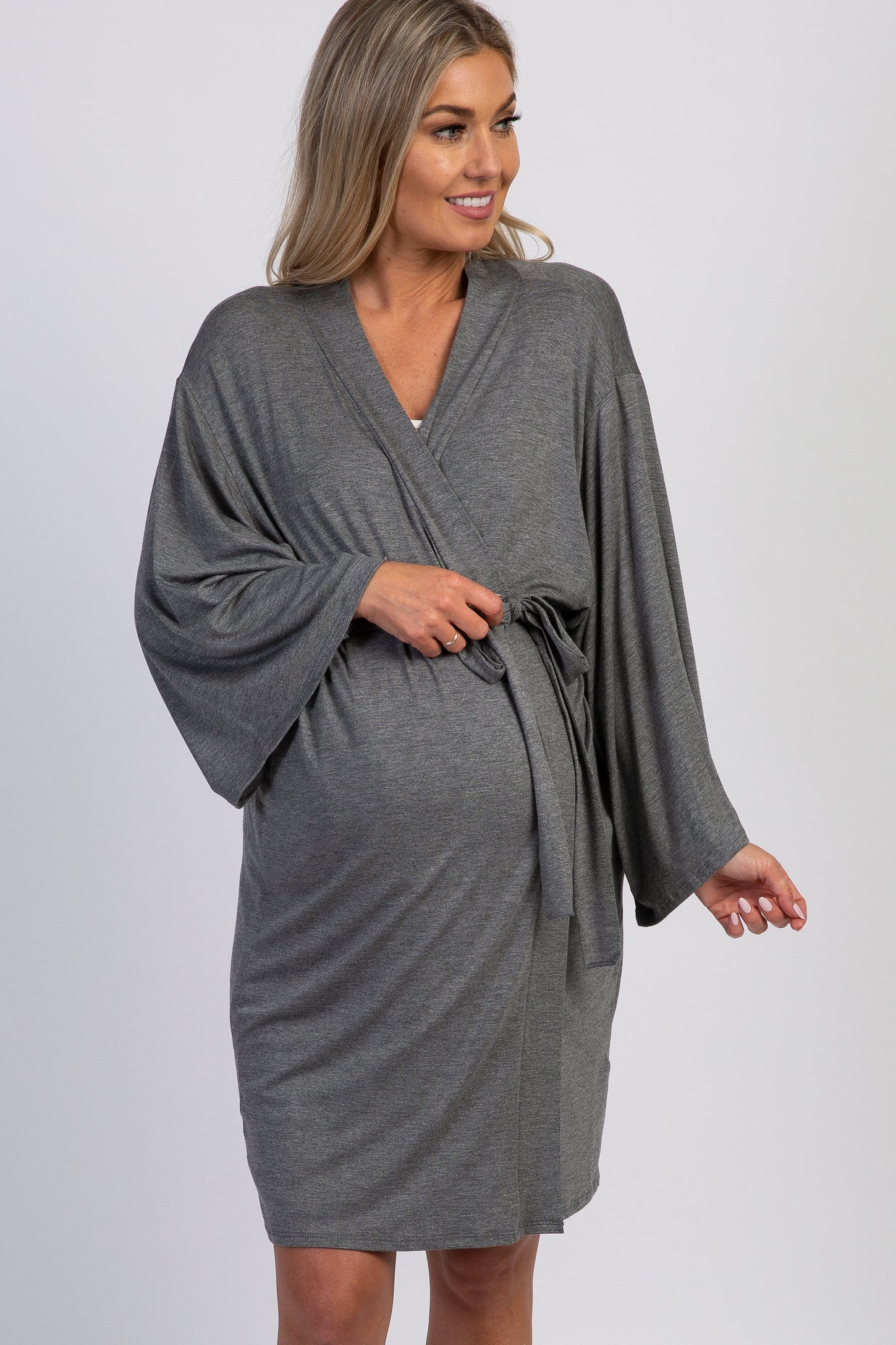 woman wearing a gray maternity wrap dress with wide sleeves and a tie waist, gently holding her baby bump