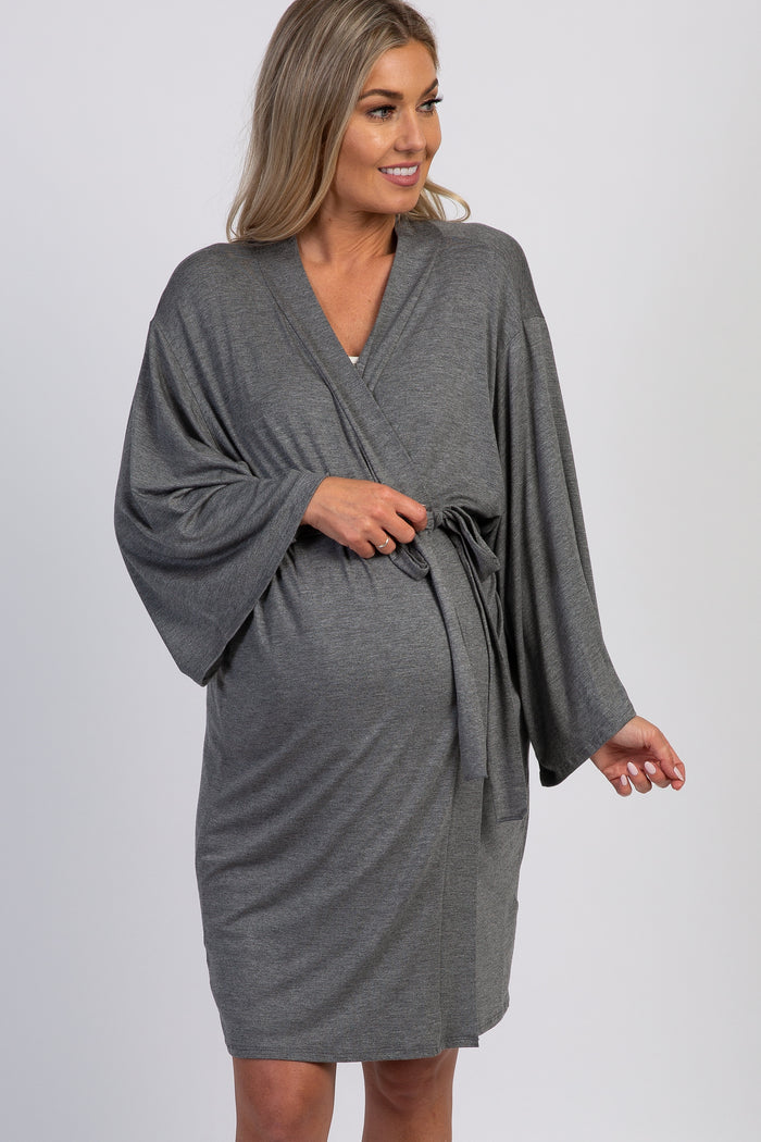 woman wearing a gray maternity wrap dress with wide sleeves and a tie waist, gently holding her baby bump