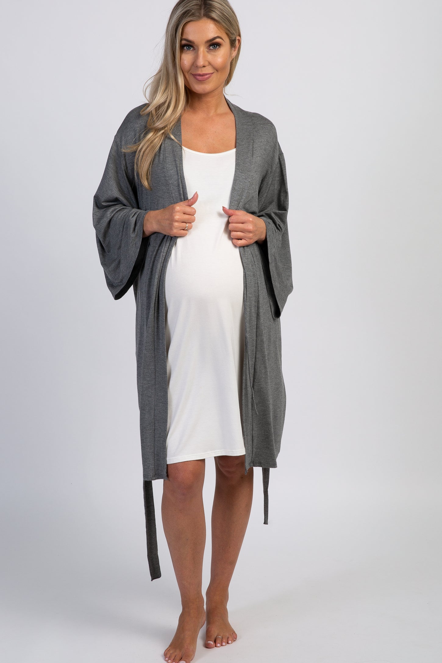woman wearing a gray maternity robe over a white maternity dress and showing her baby bump