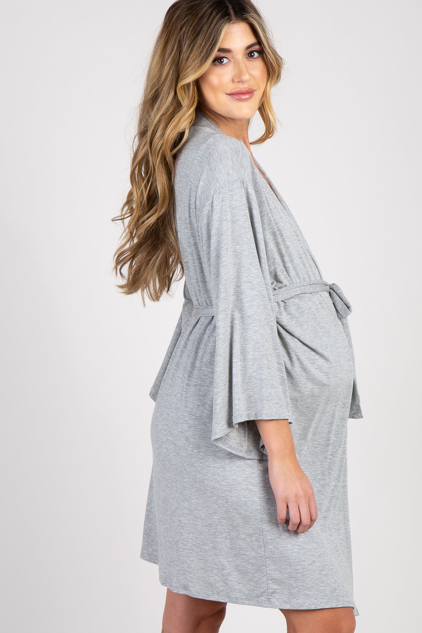 woman wearing a light gray maternity wrap dress, showcasing her baby bump while smiling and posing elegantly
