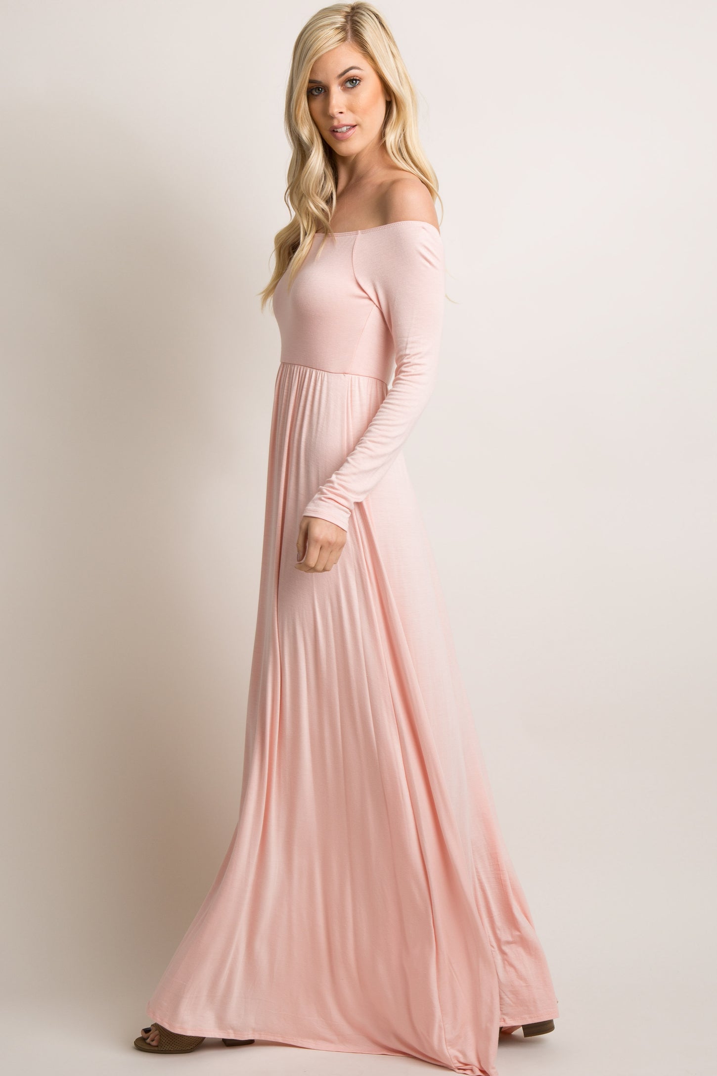 woman wearing a soft pink off-the-shoulder maxi dress with long sleeves and a flowing silhouette