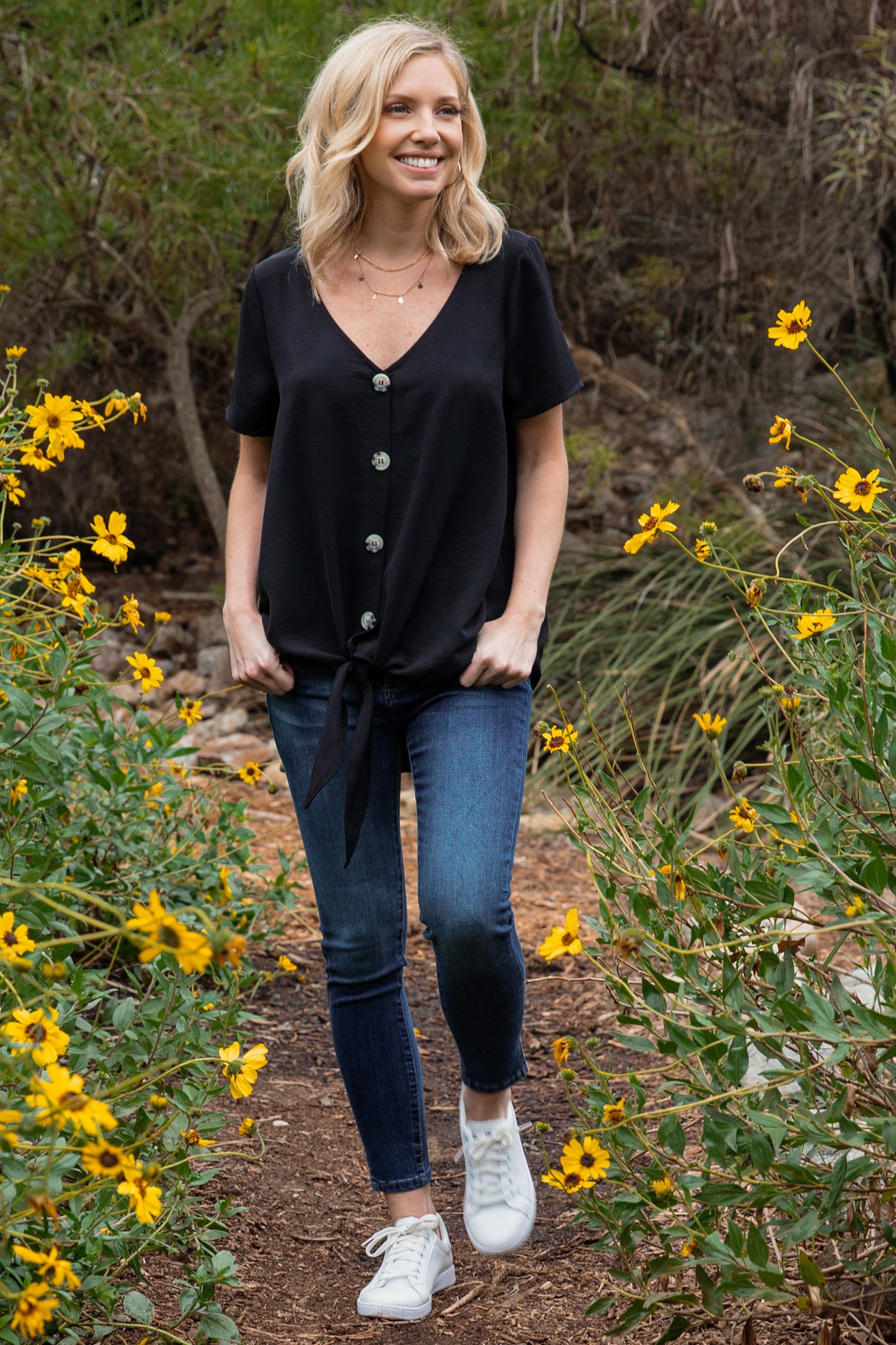 smiling woman wearing a black short sleeve v-neck top with a side tie knot and blue jeans