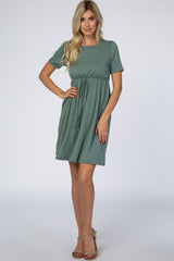 woman wearing a green short sleeve belted dress with a gathered waist and standing confidently