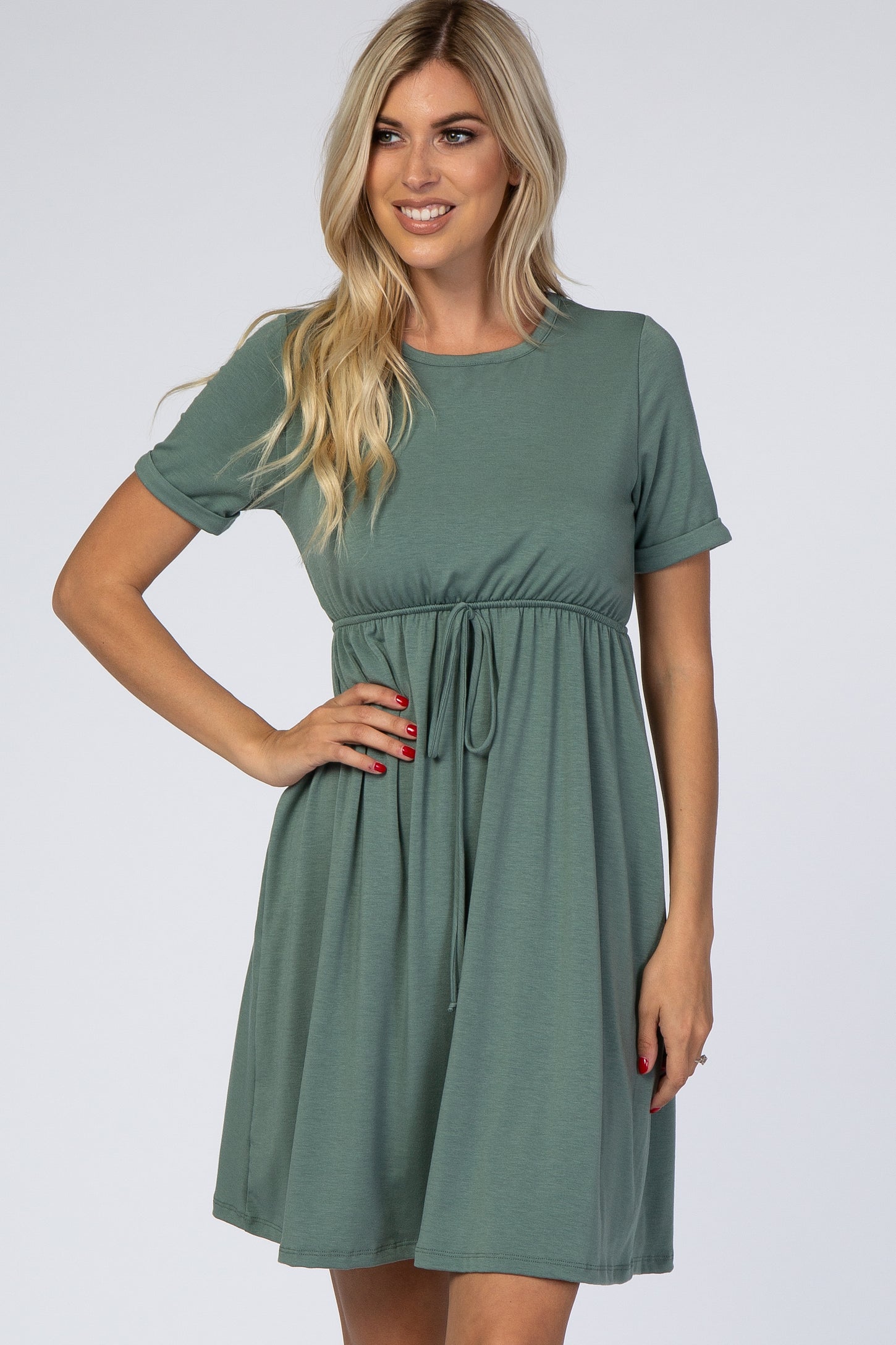woman wearing a short sleeve green drawstring waist dress with a flared skirt, smiling at the camera