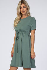 woman wearing a green short sleeve knit dress with a drawstring waist and a flared skirt
