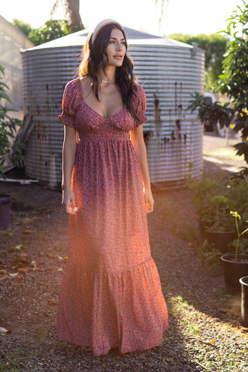 woman wearing a pink floral maxi dress with puff sleeves and a tiered skirt, standing outdoors in a garden setting