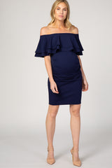 woman wearing a navy blue off-the-shoulder maternity dress with ruffle details and a visible baby bump