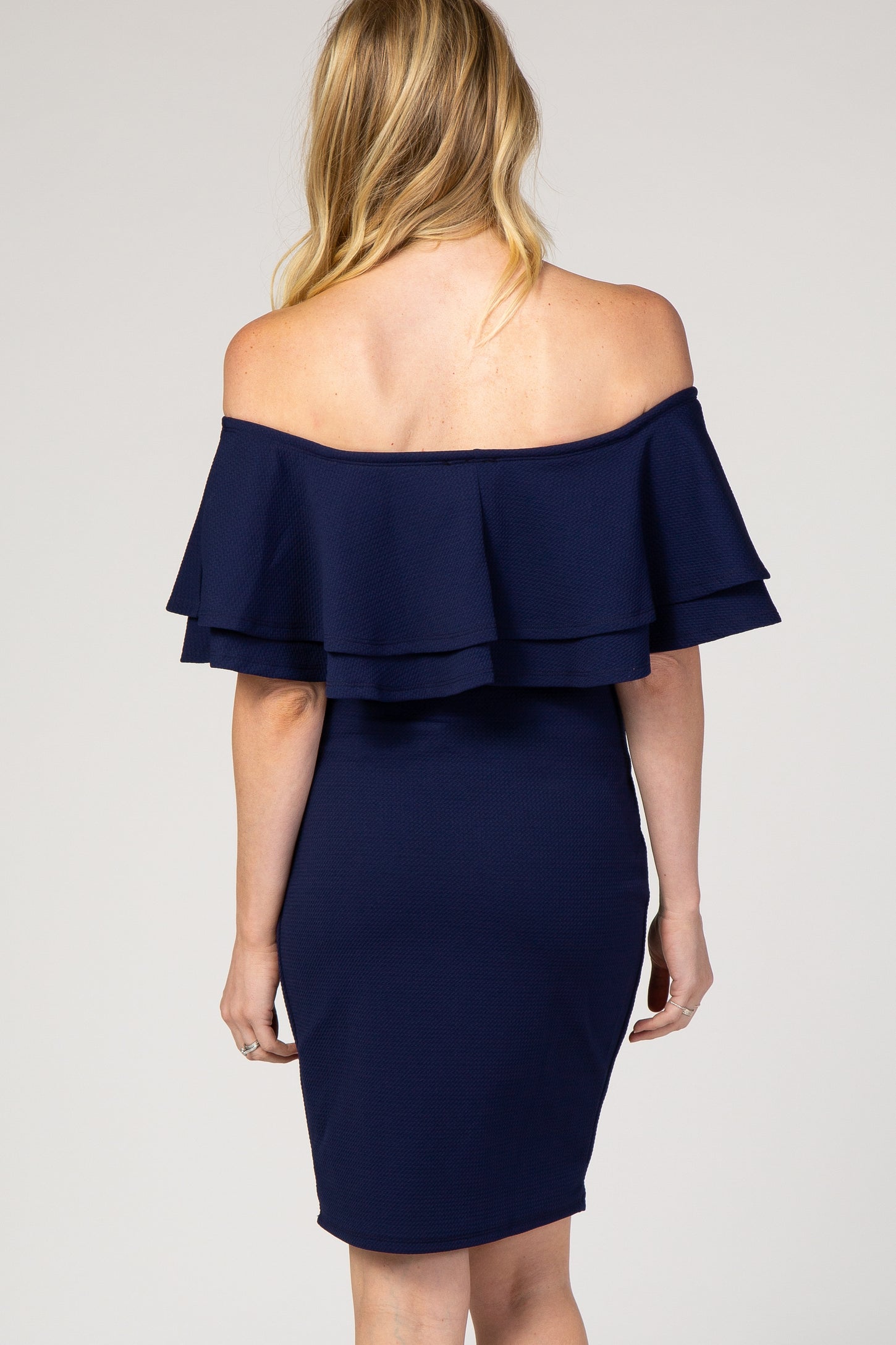 woman wearing a navy blue off-the-shoulder maternity dress with layered ruffle details on the top