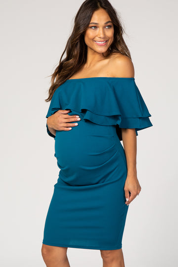 woman wearing a teal off-the-shoulder maternity dress with ruffle details and holding her baby bump