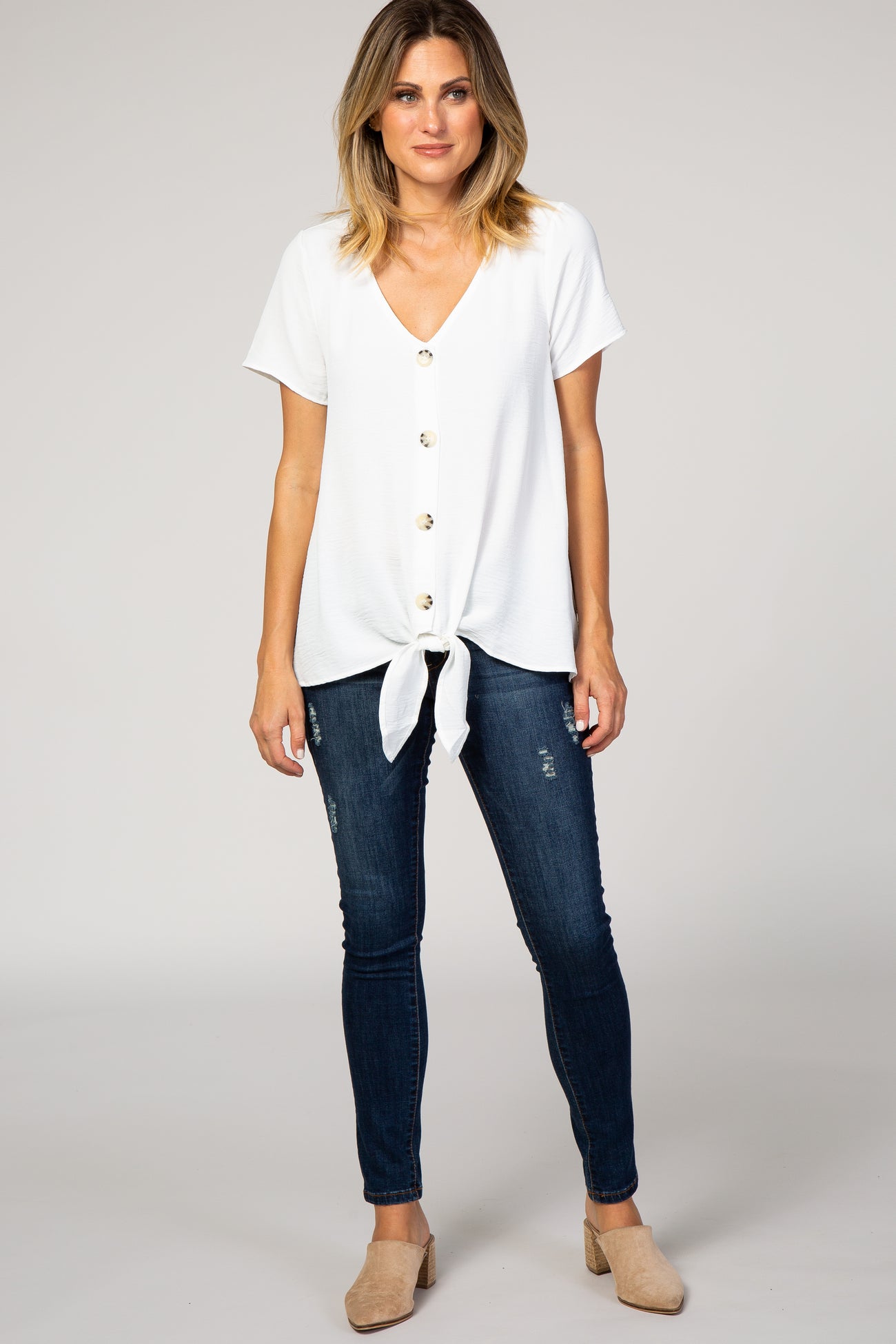 woman wearing a white short sleeve top with buttons and a front tie, paired with dark skinny jeans and beige mules
