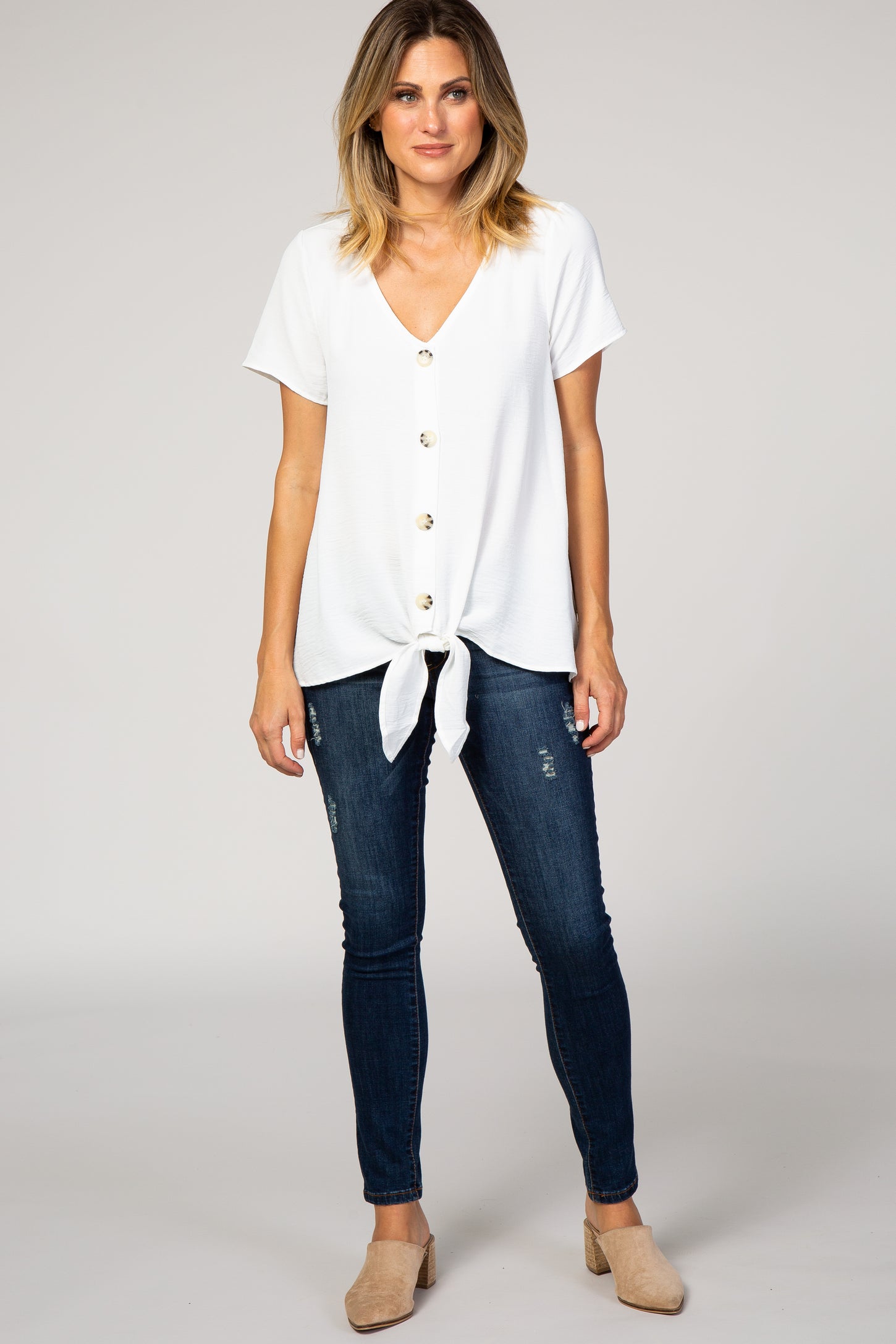 woman wearing a white short sleeve top with buttons and a front tie, paired with dark skinny jeans and beige mules
