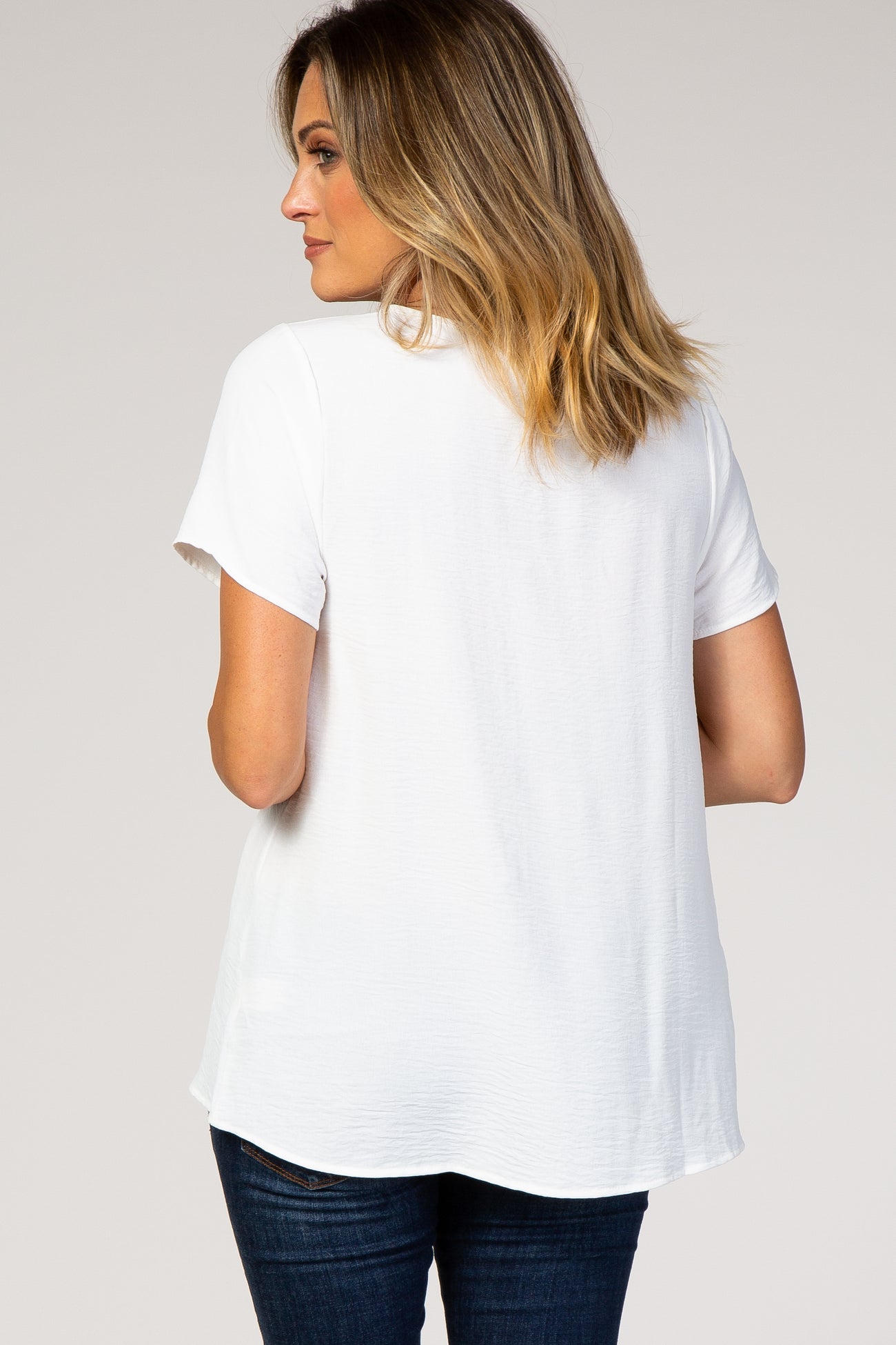 Back view of a woman wearing a white short sleeve maternity top and dark blue jeans