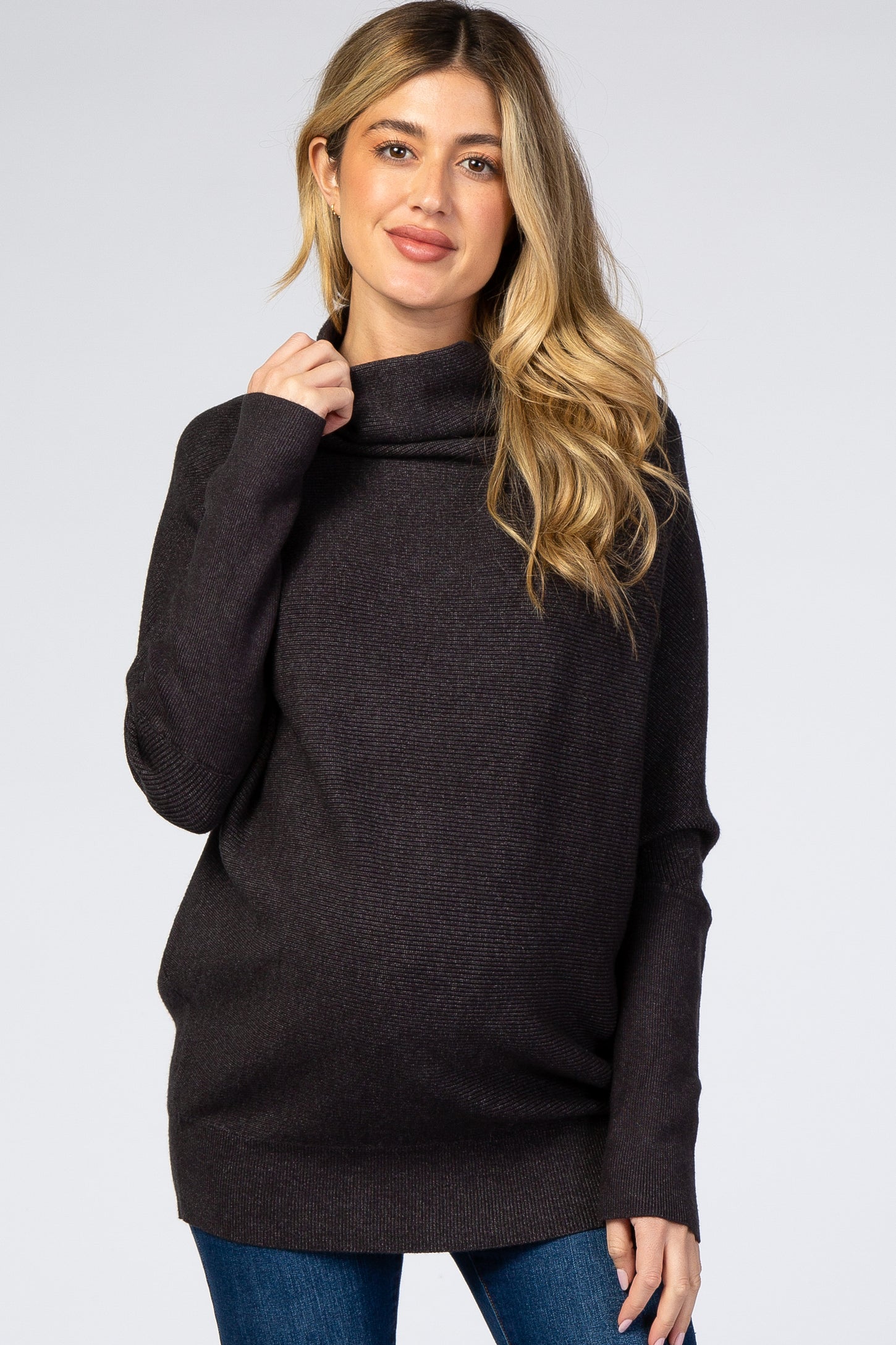 woman wearing a dark gray maternity turtleneck sweater and showing her baby bump while smiling