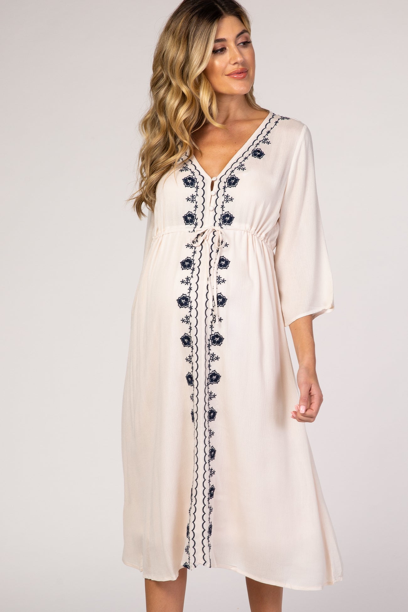 pregnant woman wearing cream maternity midi dress with navy blue floral embroidery and drawstring waist