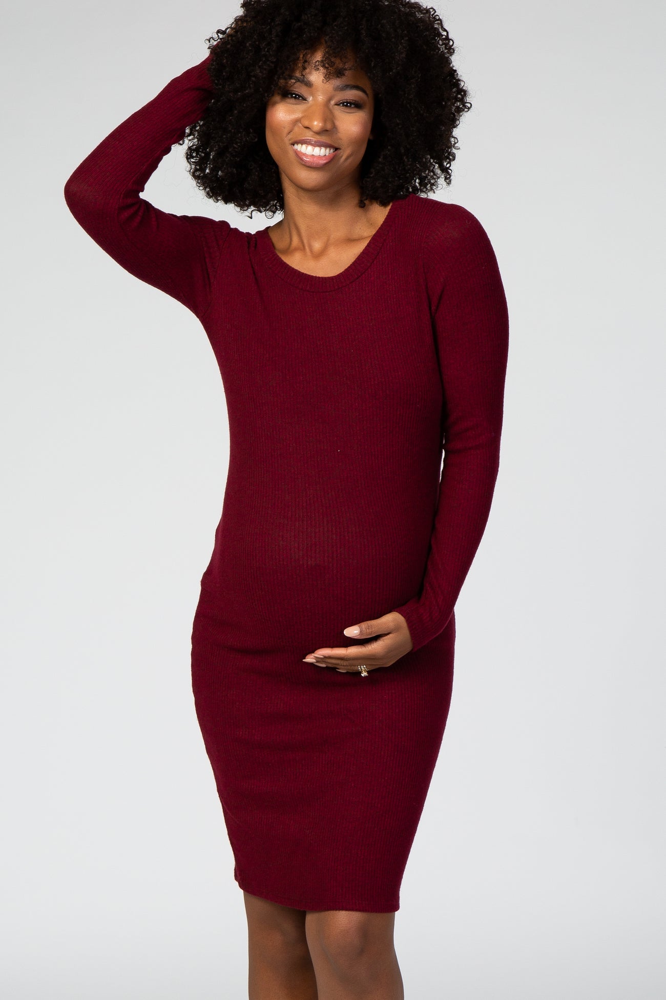 woman wearing a burgundy long sleeve ribbed maternity dress and gently holding her baby bump