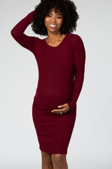 woman wearing a burgundy long sleeve ribbed maternity dress and gently holding her baby bump