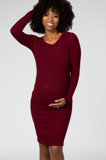 woman wearing a burgundy long sleeve ribbed maternity dress and gently holding her baby bump