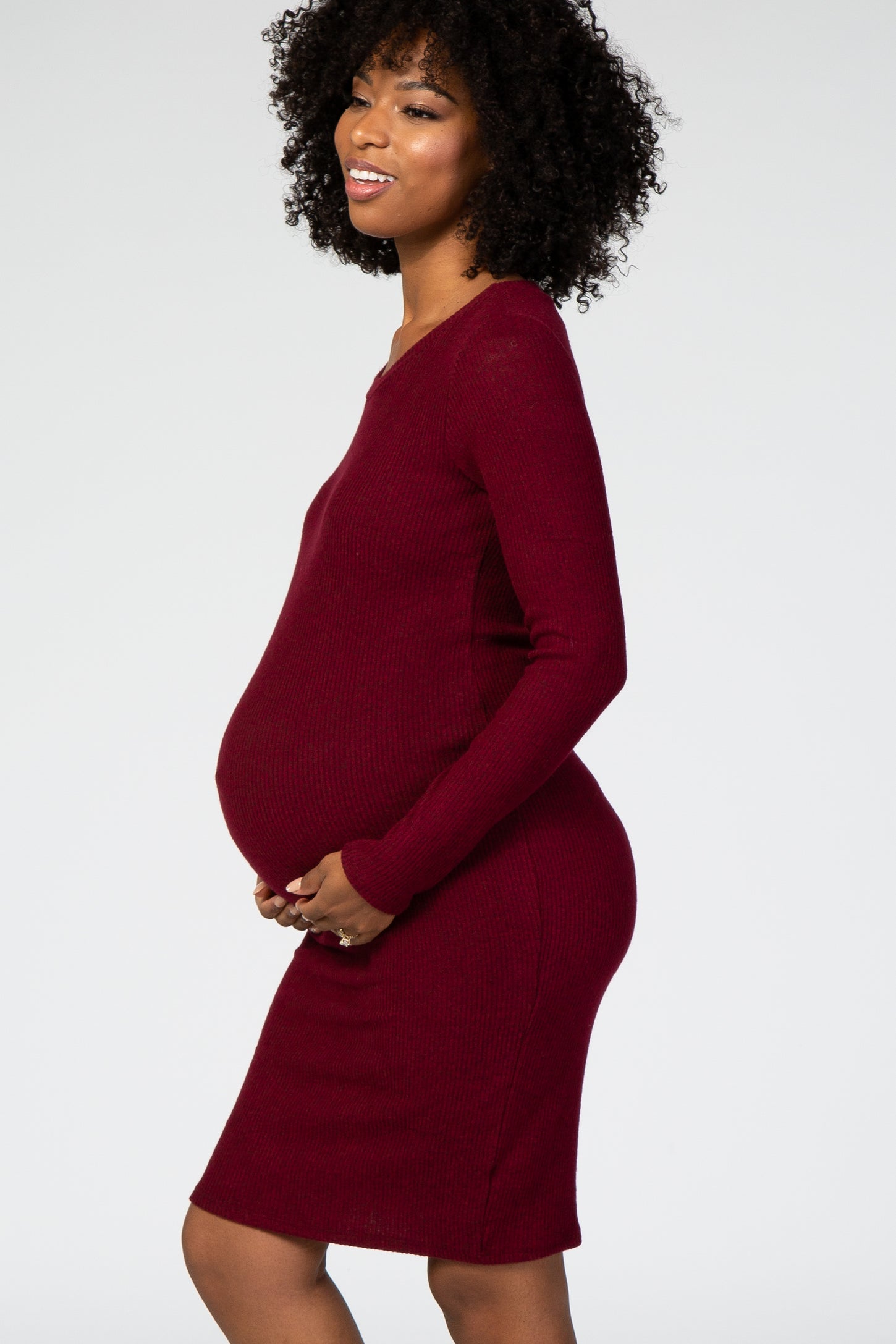woman wearing a burgundy long sleeve maternity dress and holding her baby bump