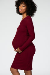 woman wearing a burgundy long sleeve maternity dress and holding her baby bump