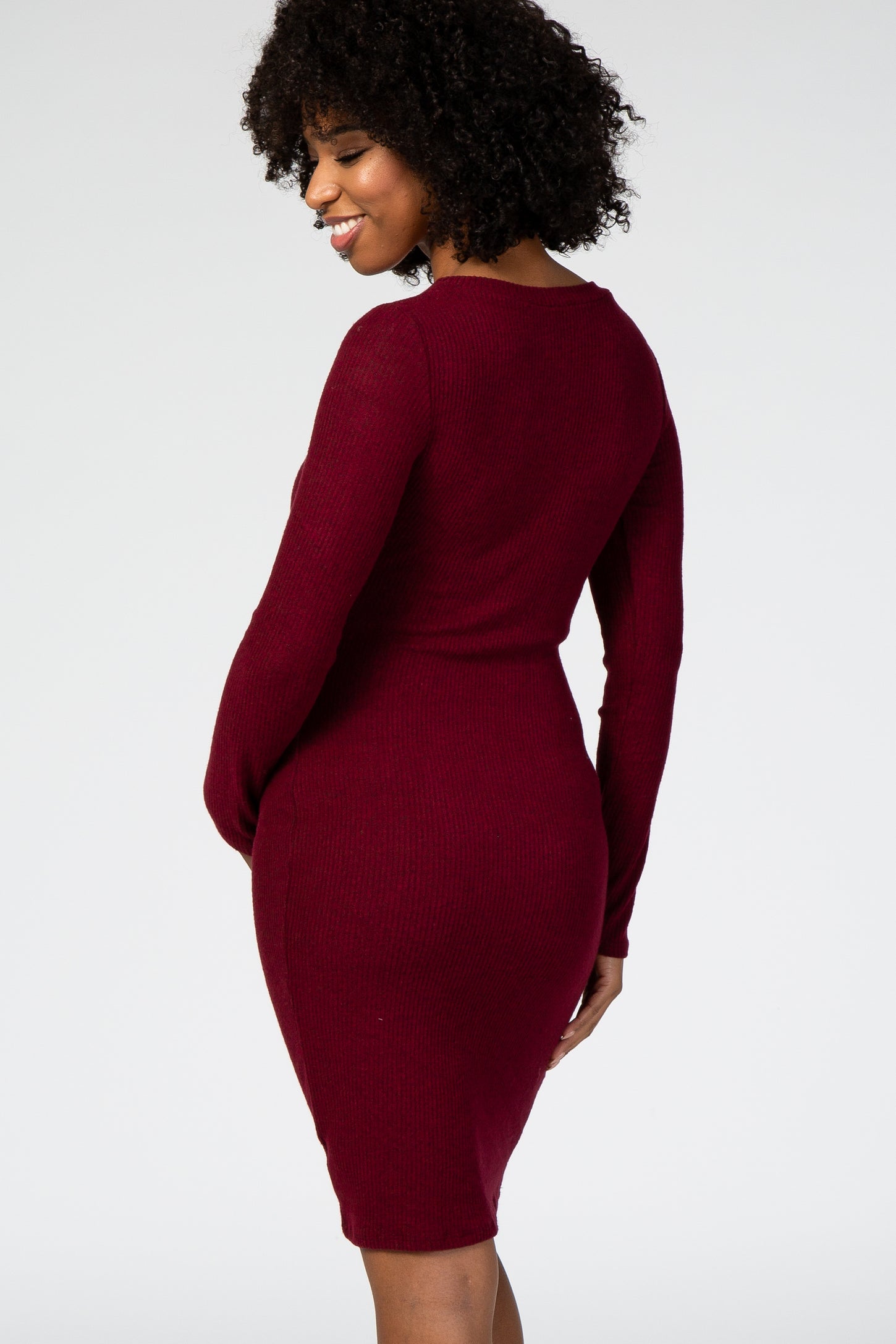 woman wearing a burgundy fitted maternity dress, showcasing a form-fitting silhouette and long sleeves