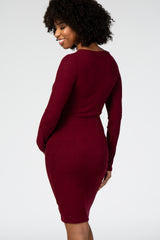 woman wearing a burgundy fitted maternity dress, showcasing a form-fitting silhouette and long sleeves