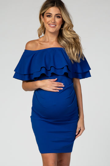 woman wearing a royal blue off-the-shoulder maternity dress with layered ruffles and holding her baby bump