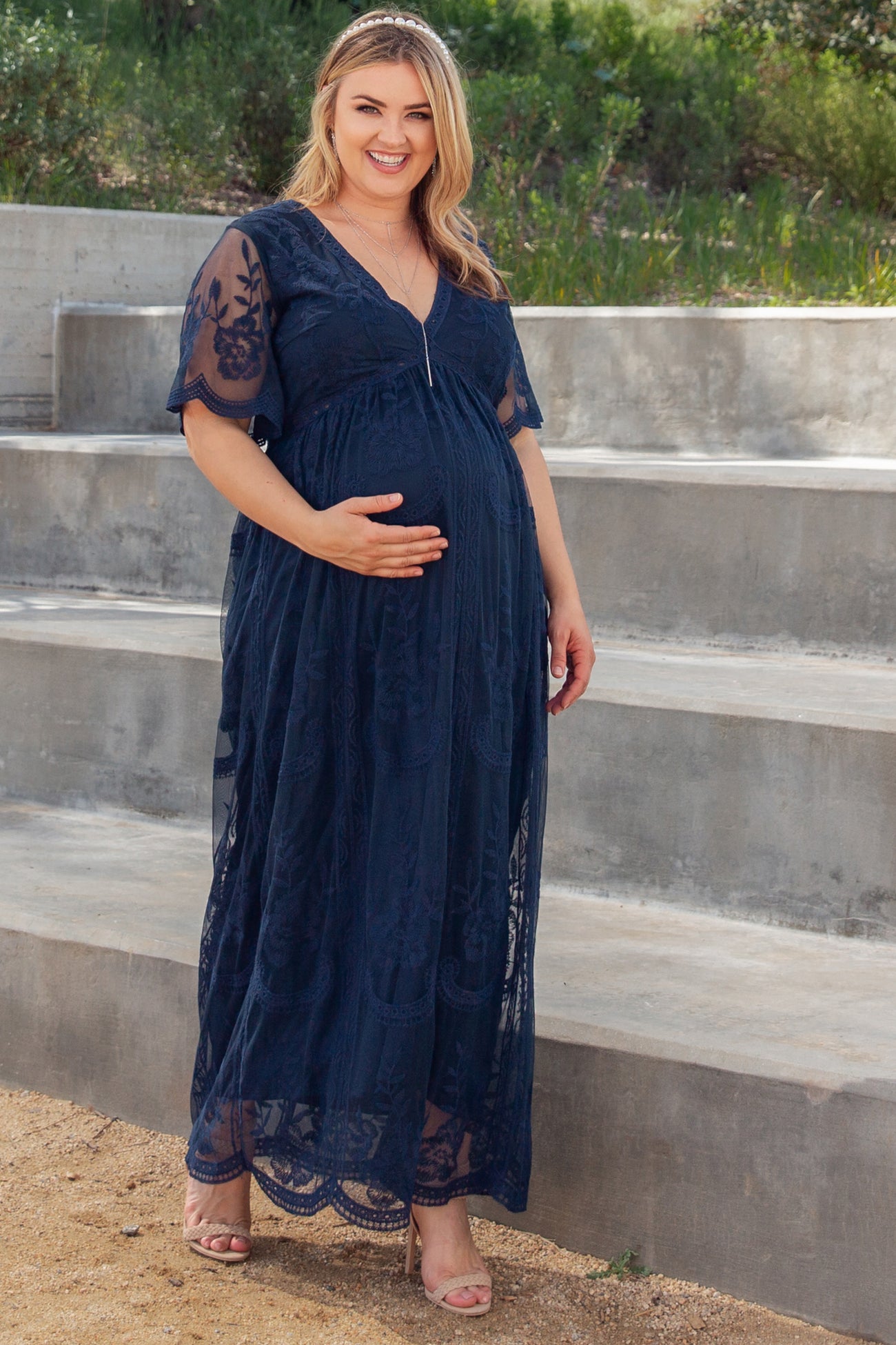 woman wearing a navy blue lace maternity gown with a v-neck and short sleeves, showcasing her baby bump