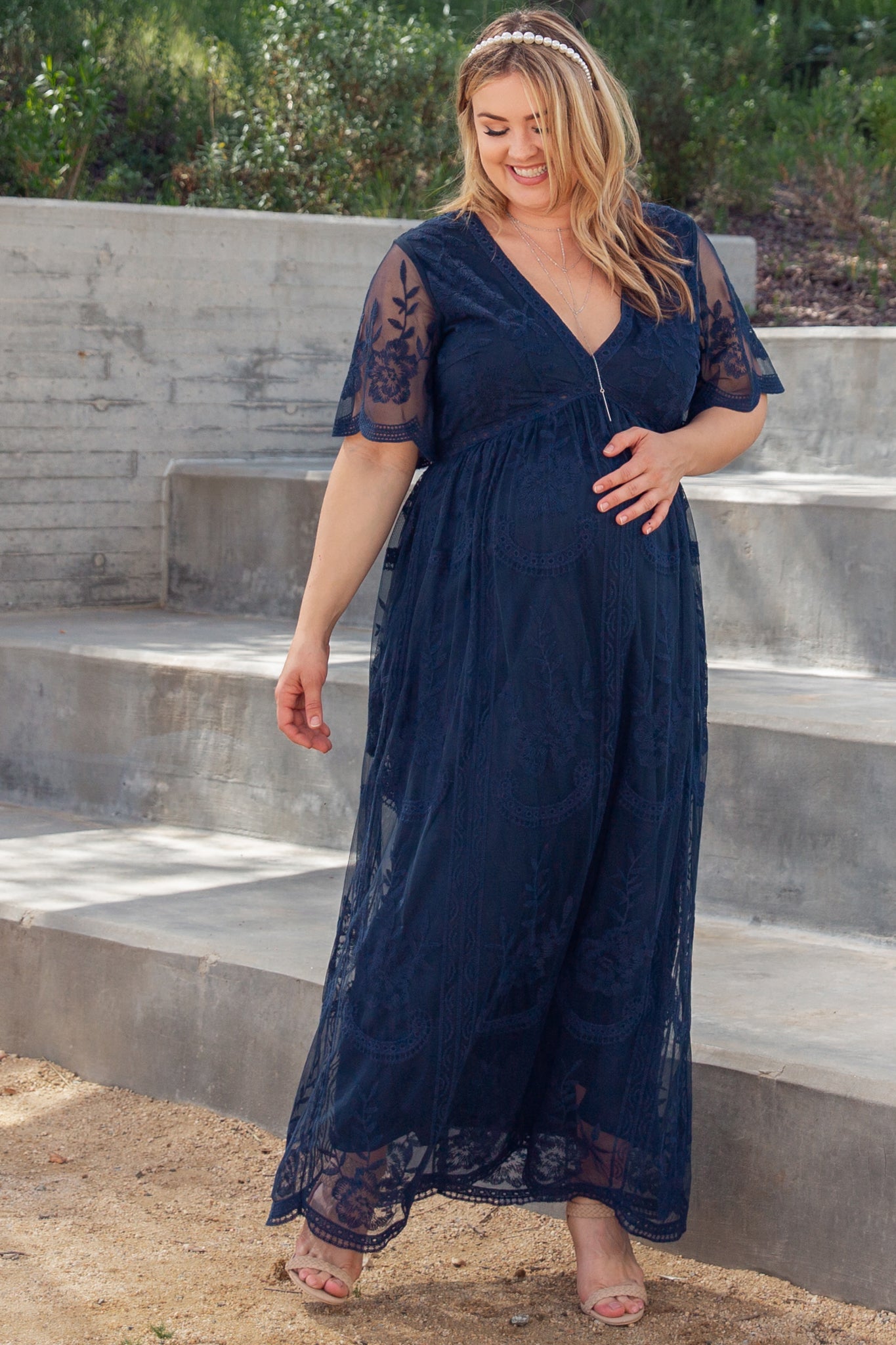 woman wearing a navy blue lace maternity maxi dress with flutter sleeves and a visible baby bump