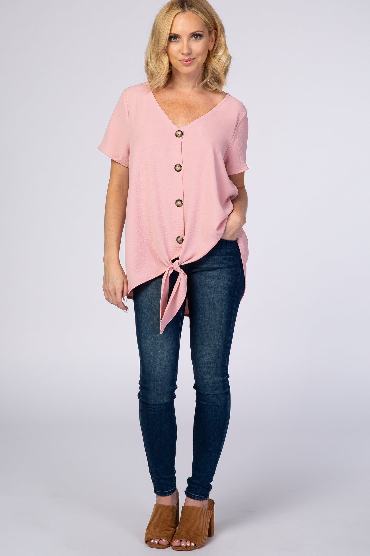 woman wearing a pink short sleeve tie-front top with buttons and jeans, standing in a casual pose