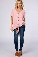 woman wearing a pink short sleeve tie-front top with buttons and jeans, standing in a casual pose