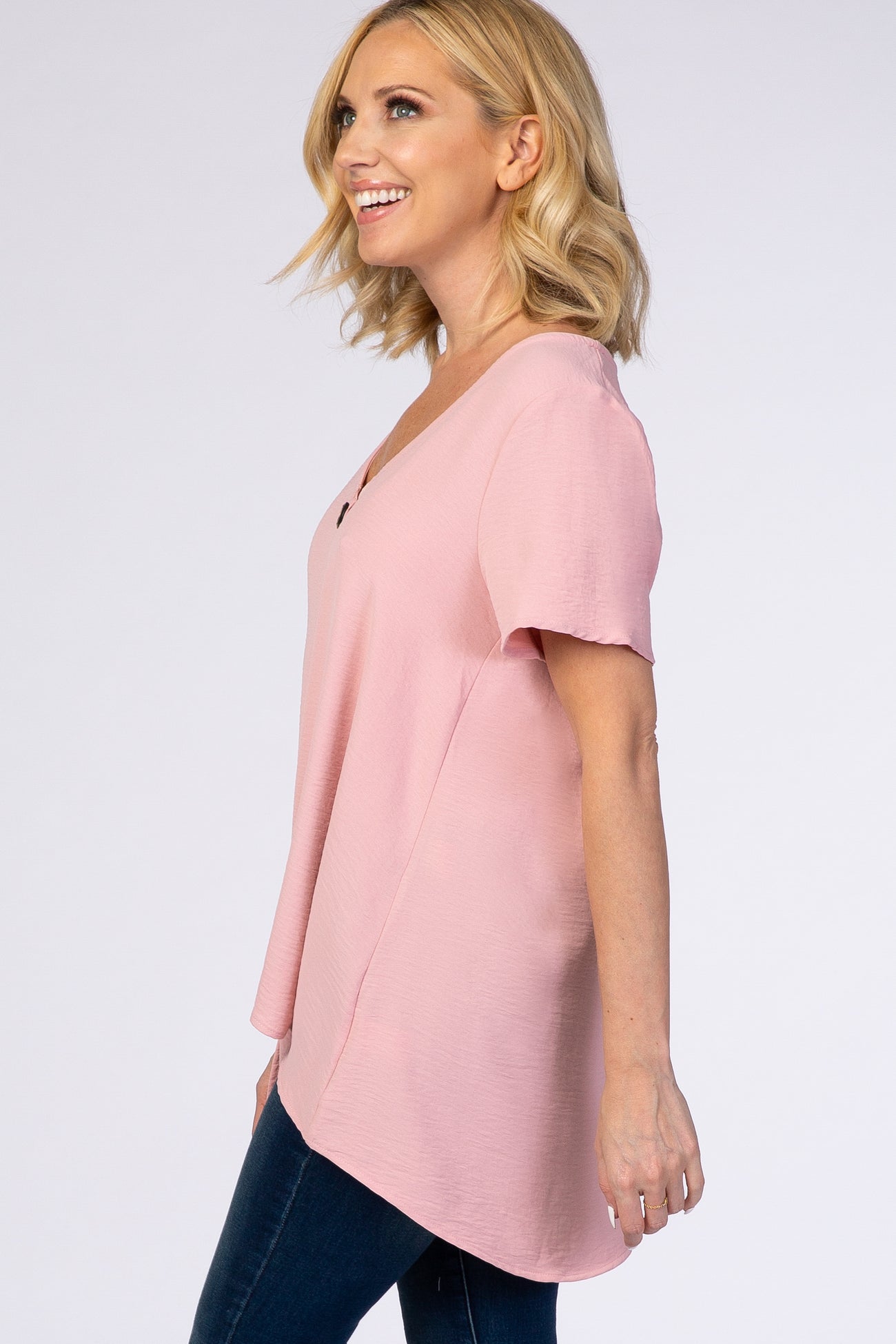 woman wearing a light pink short sleeve top with a v-neck and relaxed fit, paired with dark skinny jeans