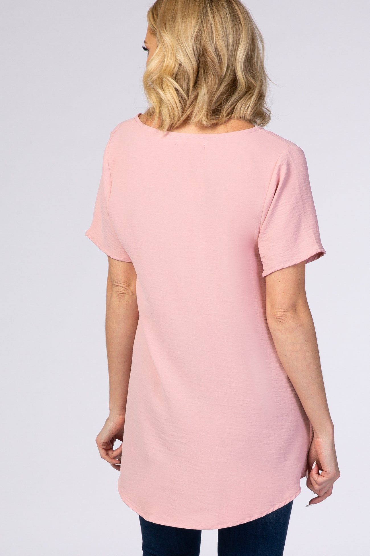 woman wearing a light pink short sleeve top with a longer back hem and a relaxed fit