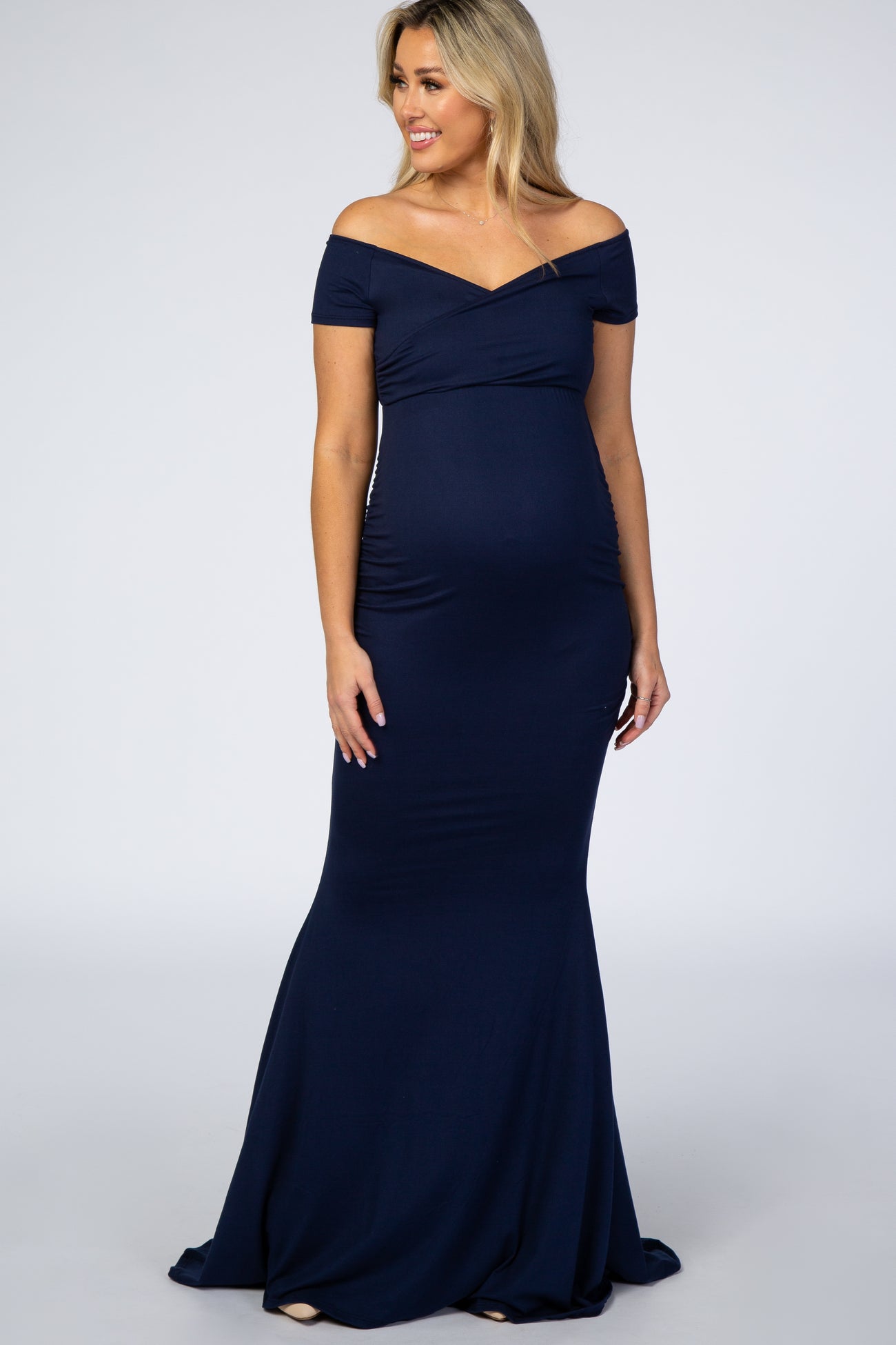 woman wearing a navy off-the-shoulder maternity gown with a fitted silhouette and a flared hem showcasing her baby bump