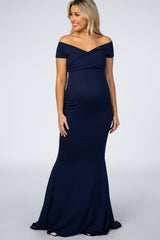 woman wearing a navy off-the-shoulder maternity gown with a fitted silhouette and a flared hem showcasing her baby bump