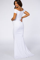 woman wearing a white off-shoulder maternity gown with ruching details and a flowing train, showing her baby bump