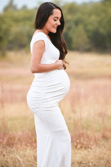 woman wearing a white maternity dress with side ruching and holding her baby bump in an outdoor setting