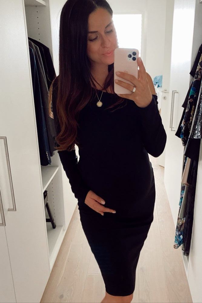 woman wearing a black long sleeve maternity dress and holding her baby bump in a mirror selfie