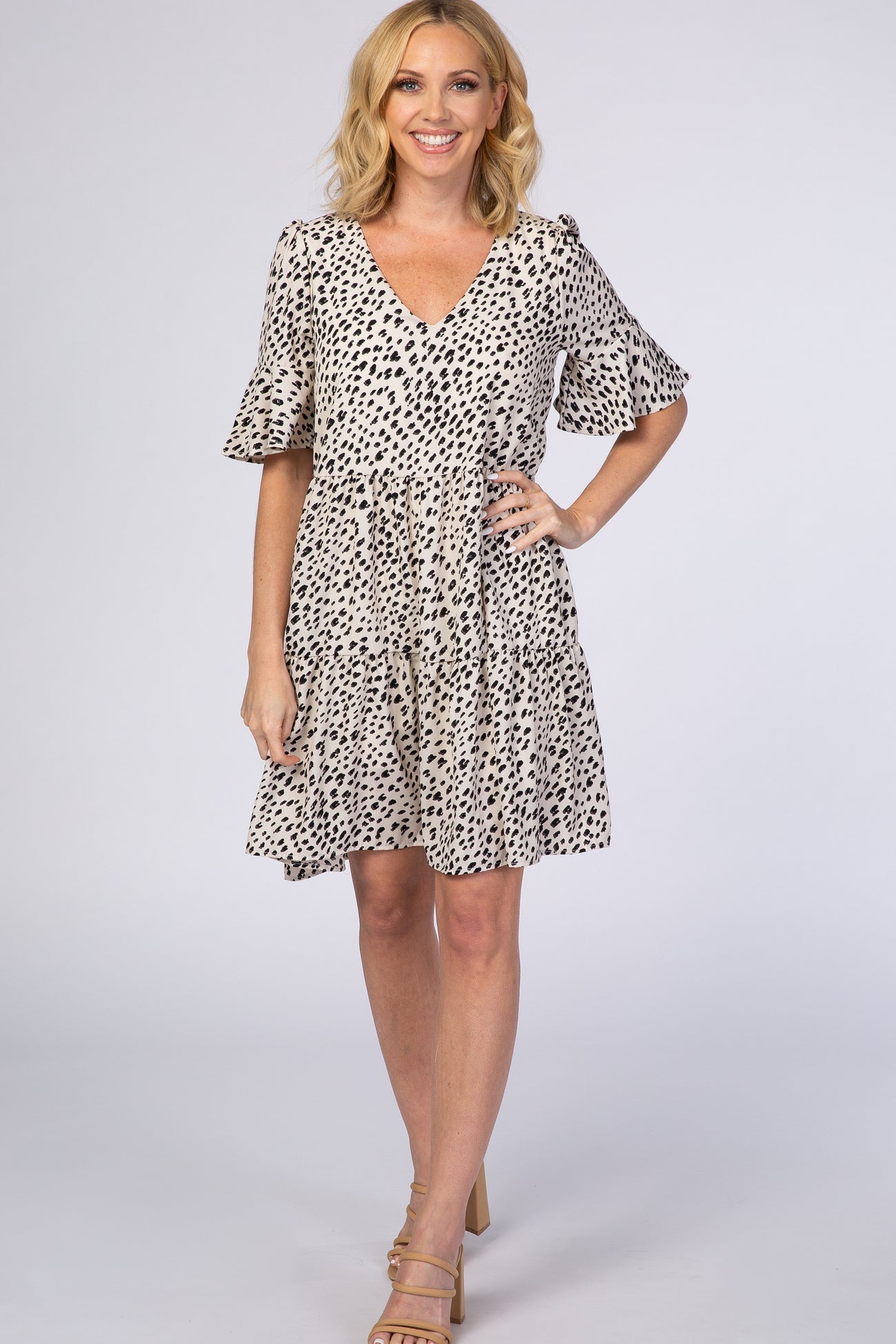 woman wearing a short beige dress with black spots and flounce sleeves